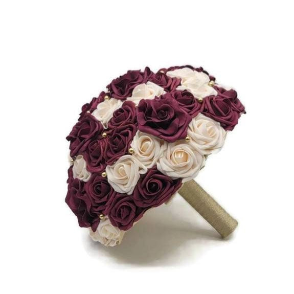 Burgundy and Cream Real Touch Roses with gold balls and avalanche roses scattered throughout. handle is made up of gold ribbon.