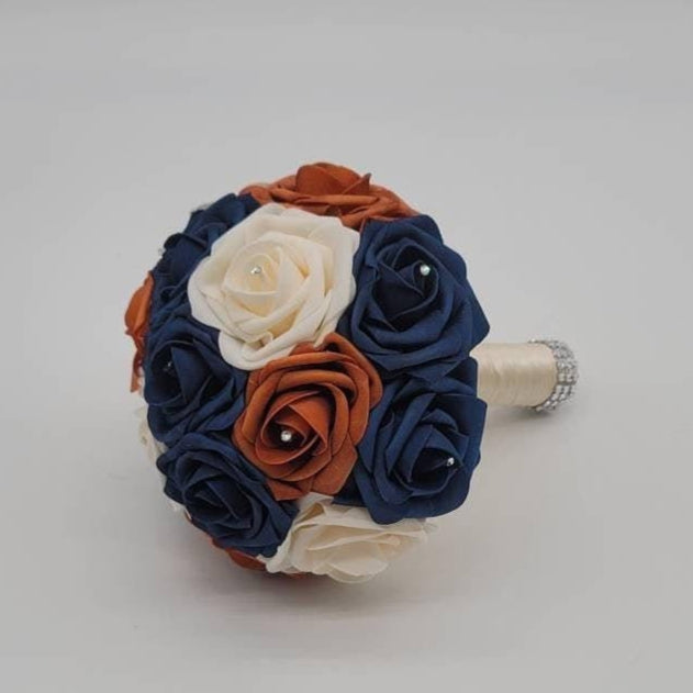 Burnt orange, cream, and navy rose bouquet with rhinestones on every rose. Handle is made up of ivory ribbon and finished with silver bling wrap.