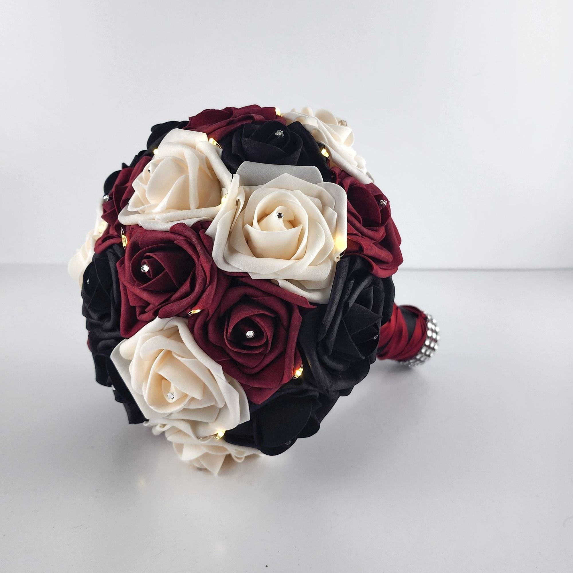 Black, Burgundy, and Cream Fairylight bouquet- Wedding bouquet-Bouquet is made using real touch roses. Handle is Blackwith a Burgundy French twist and finished with silver bling wrap. Fairy Lightsare strung through bouquet