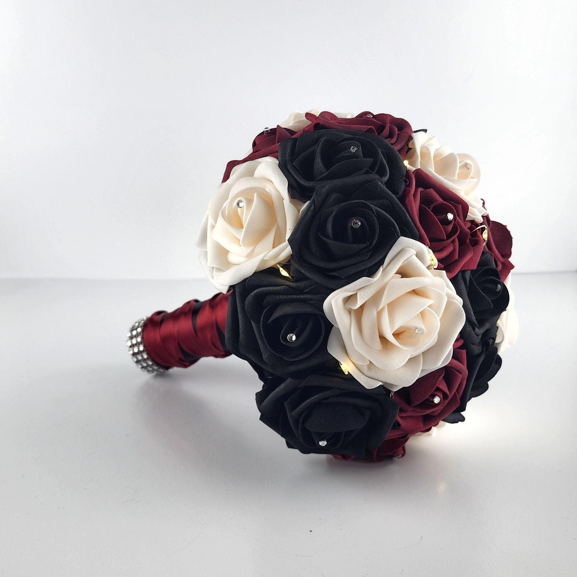 Black, Burgundy, and Cream Fairylight bouquet- Wedding bouquet-Bouquet is made using real touch roses. Handle is Blackwith a Burgundy French twist and finished with silver bling wrap. Fairy Lightsare strung through bouquet